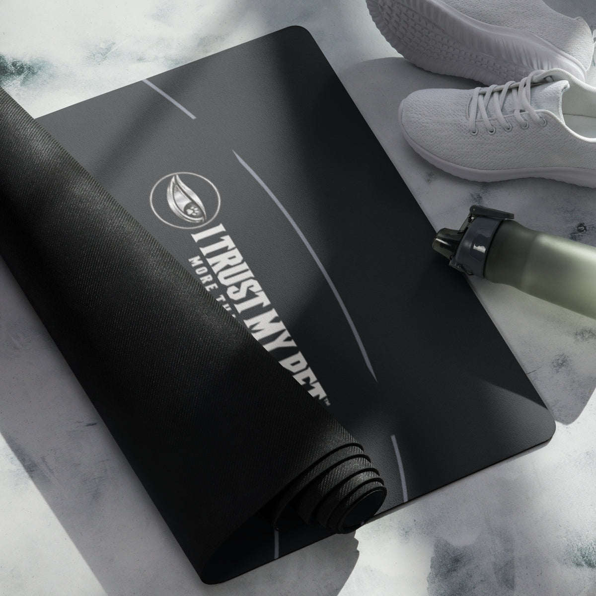 I Trust My Pet™ Inner Circle black yoga mat, rolled detail with signature logo beside shoes and a water bottle